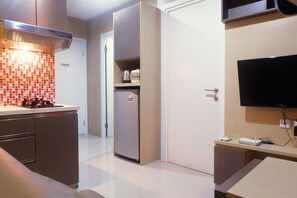 A compact kitchen with a built-in stove, a refrigerator, and a flat-screen TV mounted on the wall. - Best Price Green Pramuka Apartment (Jakarta)
