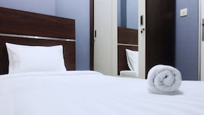 Una cama bien hecha con sábanas blancas, cabecera de madera y una toalla enrollada sobre la cama.