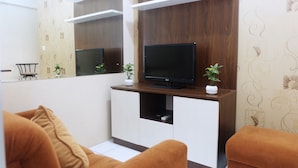 Una sala de estar moderna con un televisor de pantalla plana sobre un mueble de madera, dos plantas en macetas y un sofá marrón.