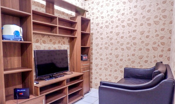 A living room with a TV on a wooden stand, a sofa, and a patterned wallpaper. - Strategic Menteng Square Apartment (Jakarta)