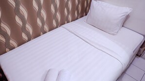 A neatly made bed with white linens and two rolled towels, a plain white pillow, and a patterned curtain in the background. - Warm Cozy Menteng Square Apartment (Jakarta)