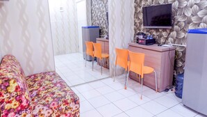 A hotel room with a floral sofa, a wooden desk with two orange chairs, a television, and a water dispenser. - Warm Cozy Menteng Square Apartment (Jakarta)
