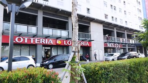 A multi-story building with balconies, a visible storefront with signage, and parked cars.