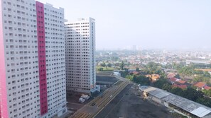 A high-rise building with a distinctive pink and white facade, a large open area with a road and railway tracks, and a view of a cityscape with various buildings and greenery.