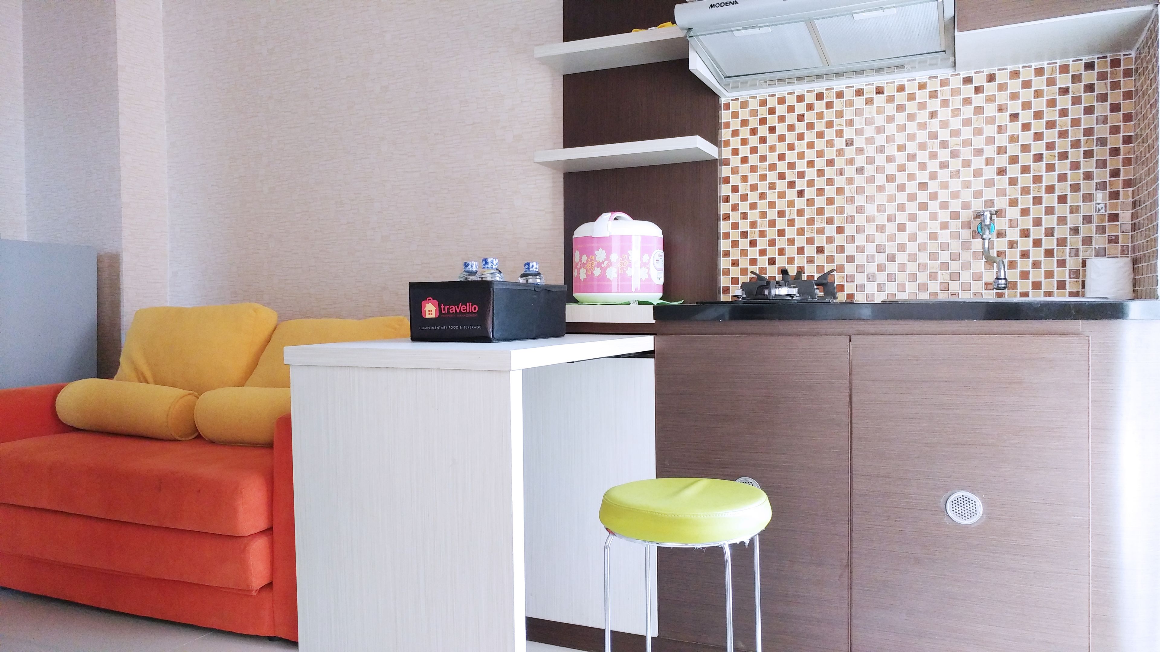 Una kitchenette compacta con mostrador blanco, un taburete pequeño y una cafetera de viaje.