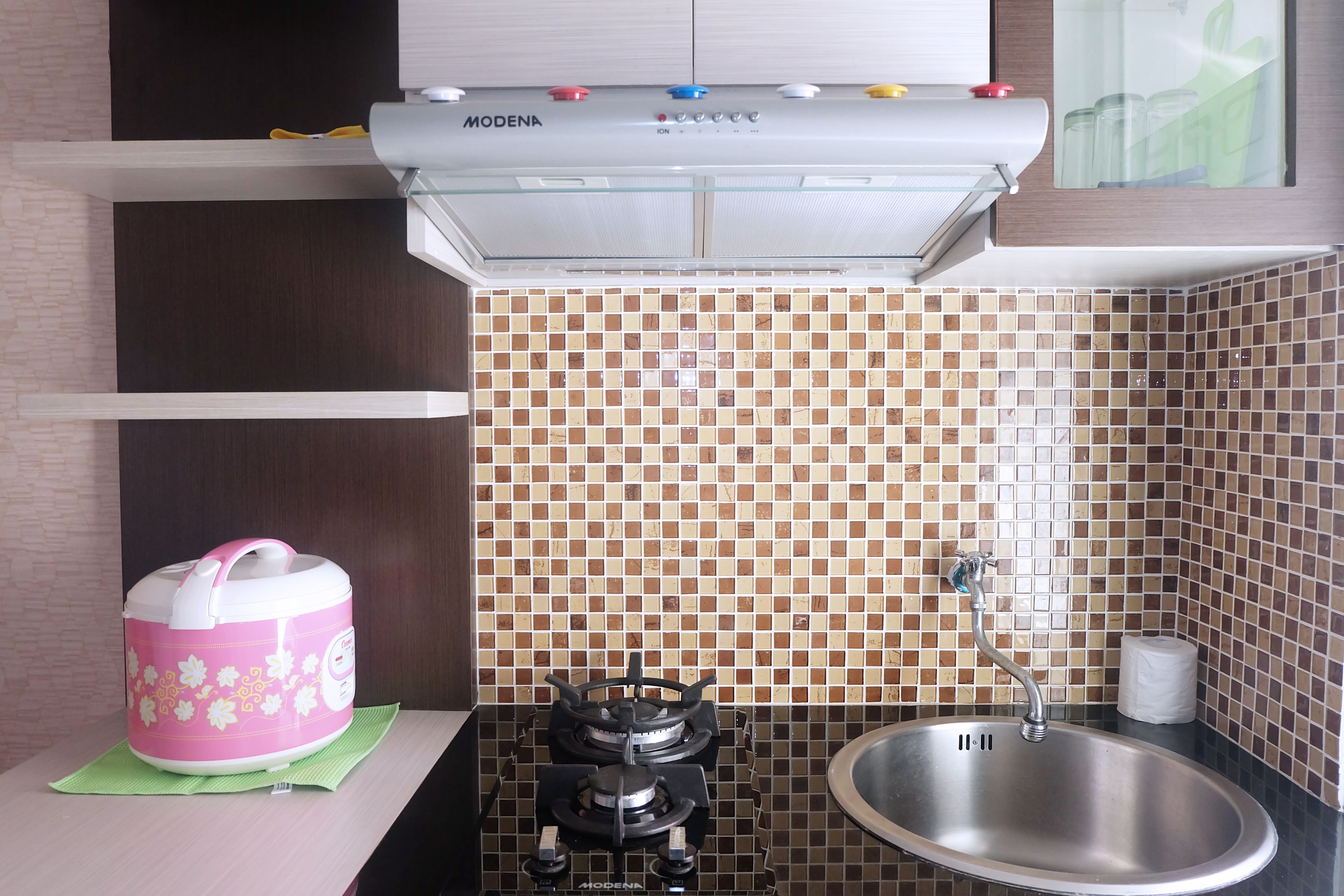 A kitchen with a gas stove, a sink, and a pink rice cooker on the counter.