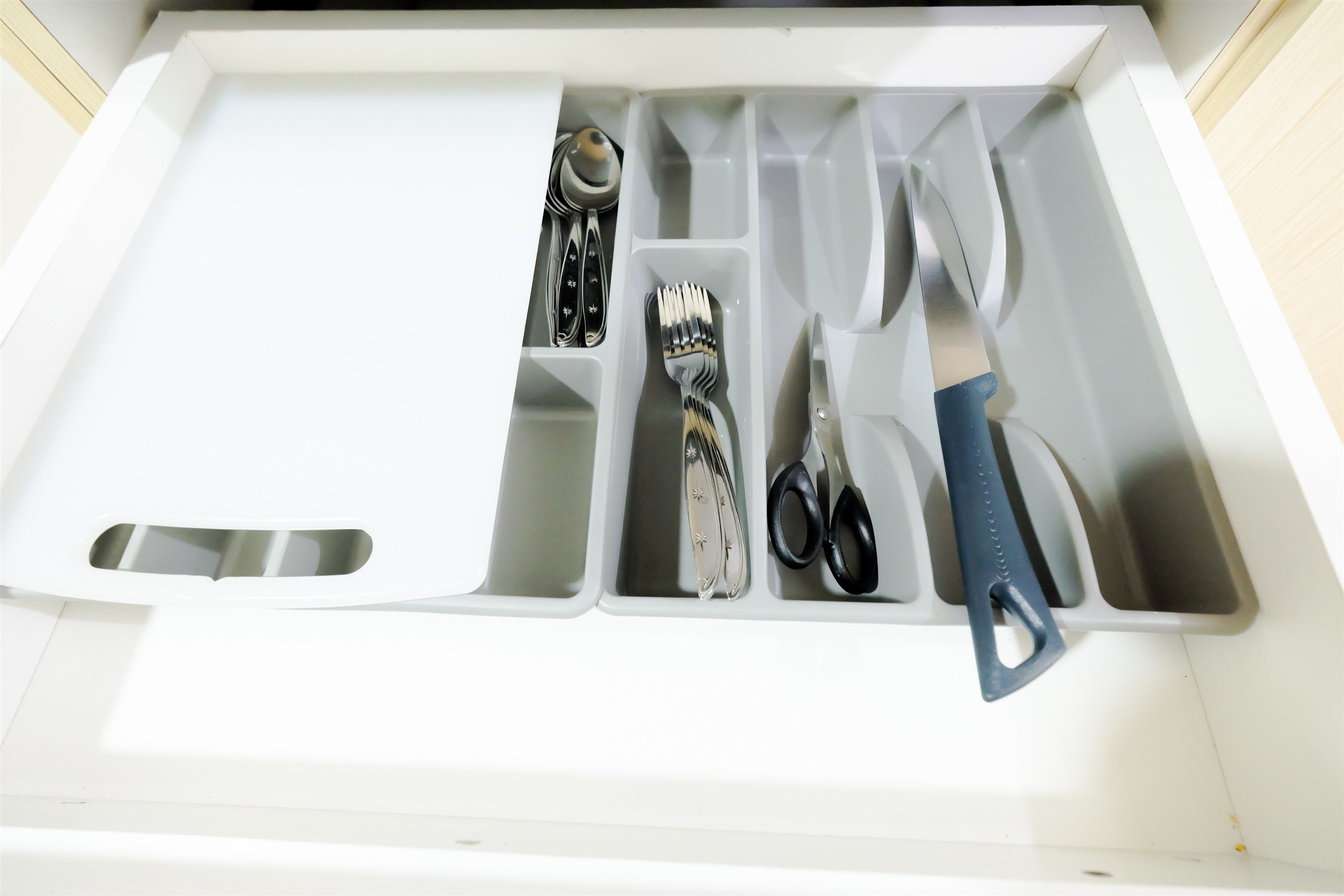 A drawer with compartments containing a spoon, fork, knife, scissors, and a pair of pliers.