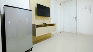 A hotel room with a flat-screen TV mounted on the wall, a built-in wooden cabinet below, and a white door. - Simply & Clean Bassura City Apartment (Jakarta)
