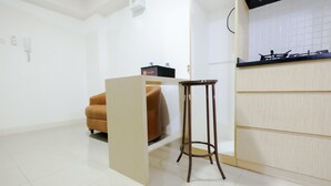 A modern kitchen with a wooden countertop, a small stool, and a beige sofa. - Simply & Clean Bassura City Apartment (Jakarta)