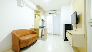 A modern living room with a sofa, a TV, and a small desk. - Simply & Clean Bassura City Apartment (Jakarta)