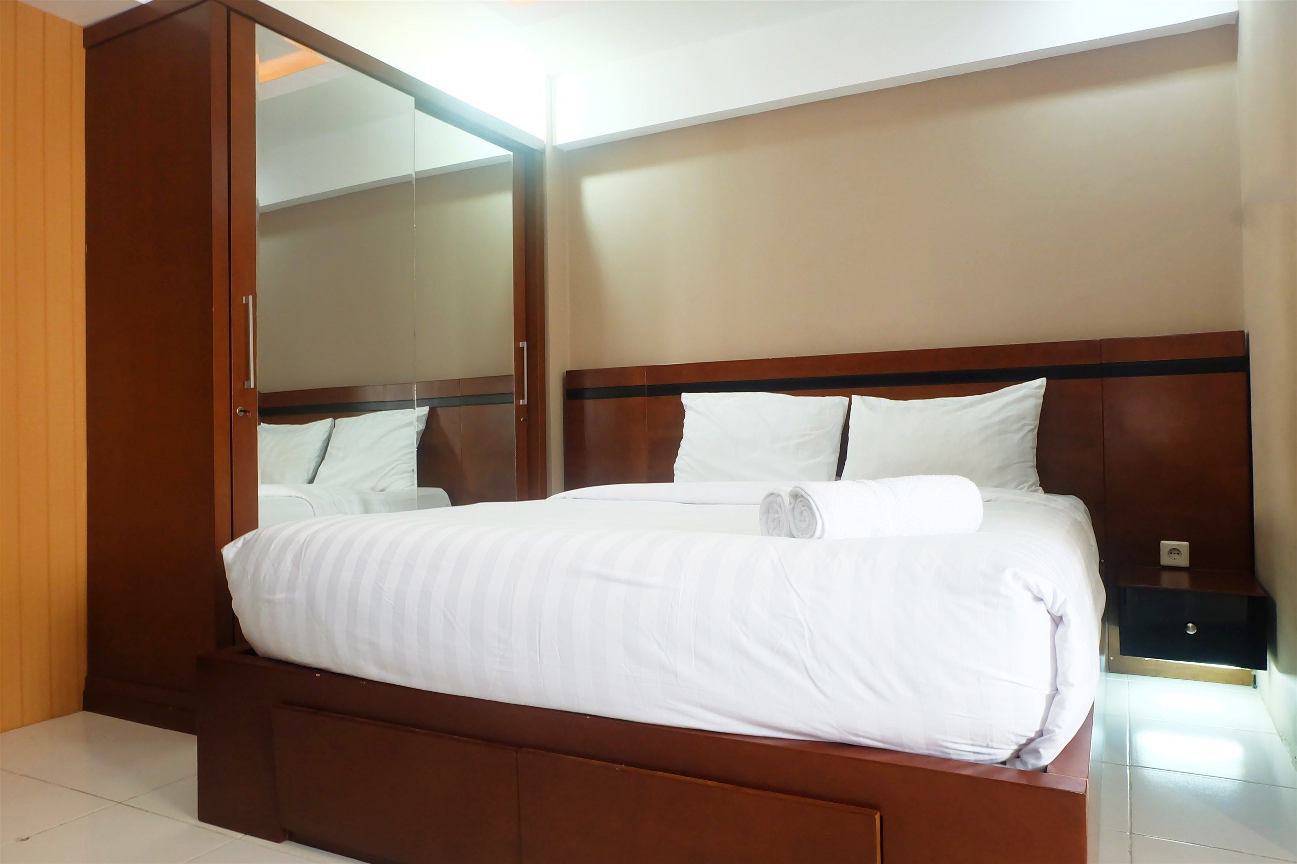 Una cama bien hecha con sábanas blancas, un cabecero de madera y una mesita de noche con toma de corriente.