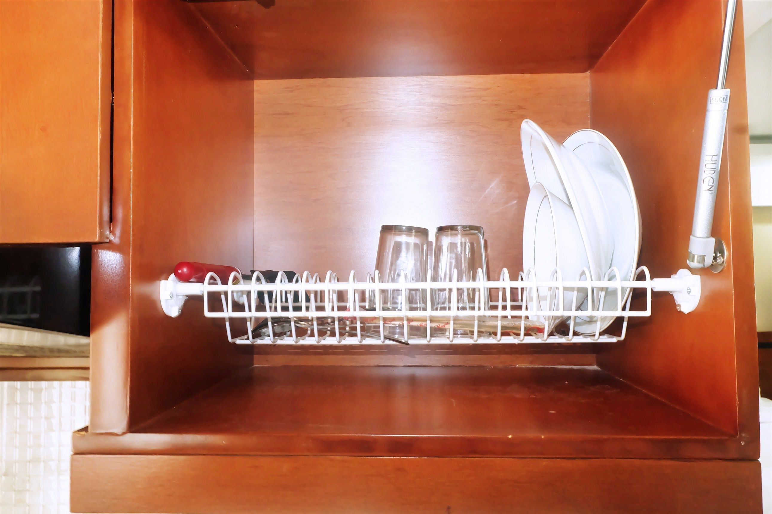 A kitchen with a wooden cabinet, a dish rack with glasses and plates, and a white appliance.