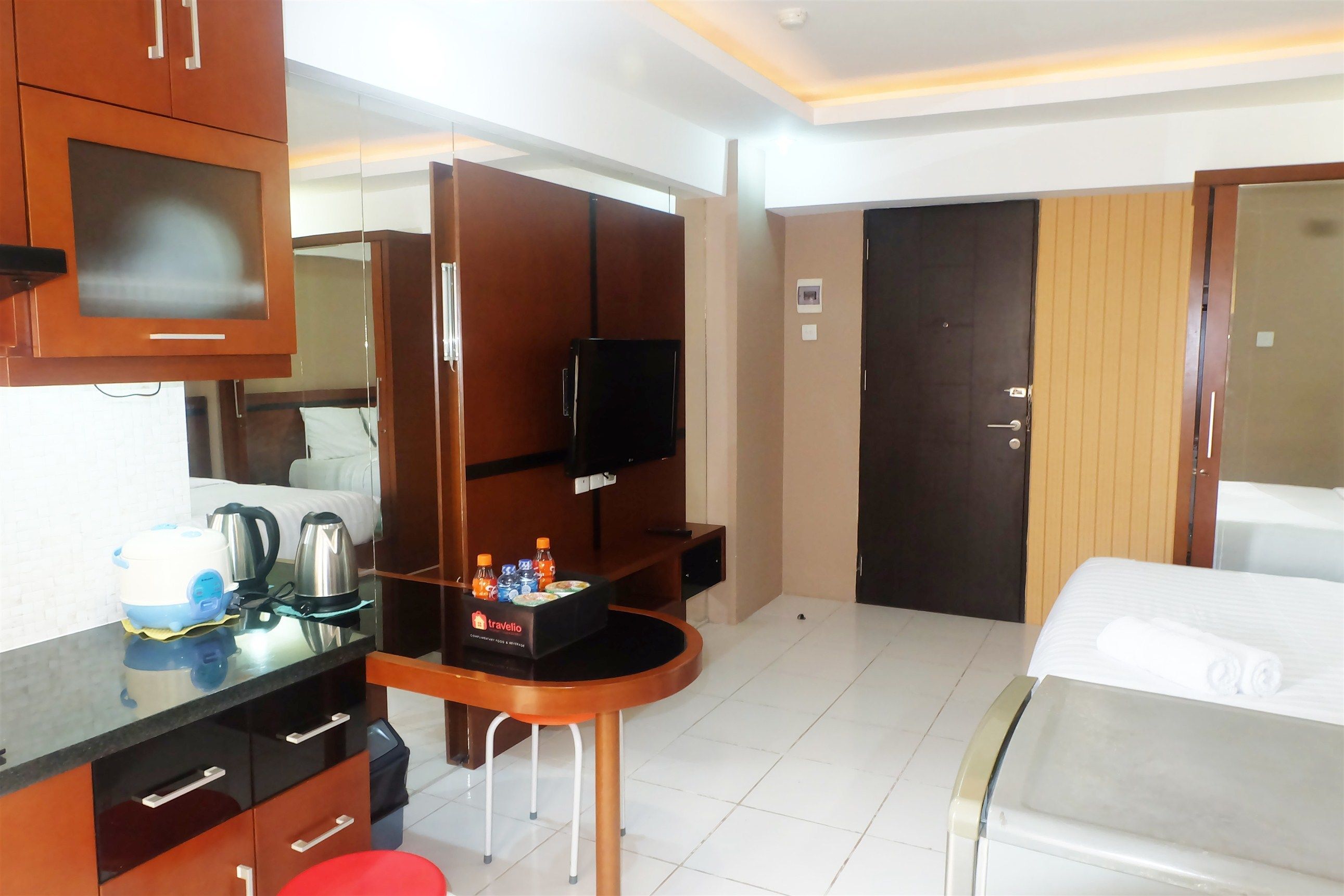 A hotel room with a bed, a desk with a computer, a TV, and a minibar.