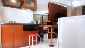 A compact kitchen with wooden cabinets, a gas stove, a coffee maker, and two stools. - Kebagusan City Simple And Affordable Studio (Jakarta)