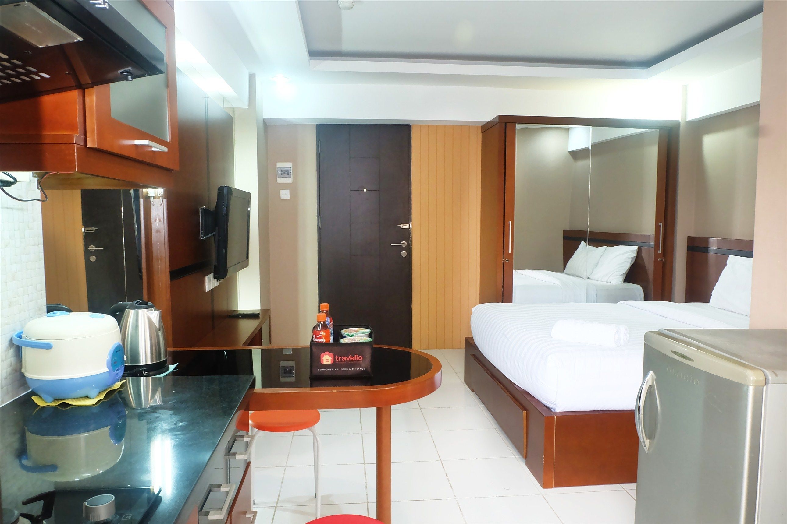 Habitación de hotel pequeña con cama, una mesita con hervidor y una botella, refrigerador y microondas.