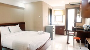 A hotel room with a bed, a desk, a chair, a kitchenette, and a window. - Kebagusan City Simple And Affordable Studio (Jakarta)