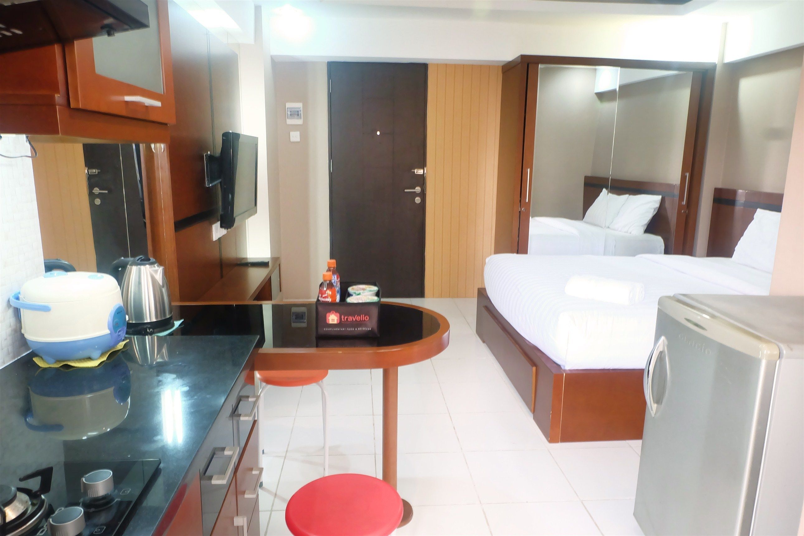 A compact hotel room with a kitchenette, a bed, and a small seating area.