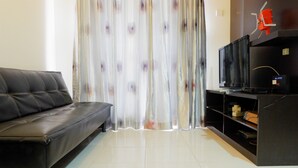 Un salon avec un canapé en cuir noir, un téléviseur posé sur un meuble et un rideau orné d’un motif floral.