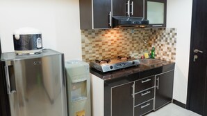 Une cuisine compacte équipée d’un réfrigérateur, d’un distributeur d’eau, d’une cuisinière et de meubles de rangement de couleur sombre.