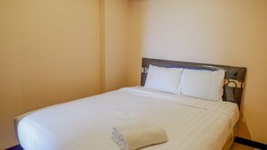Un lit bien fait, avec des draps blancs et une serviette enroulée, une tête de lit en bois et un mur sobre.