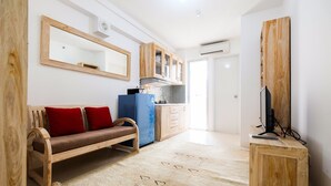 A compact living space with a sofa, a small kitchenette, a television on a wooden stand, and a mirror on the wall.