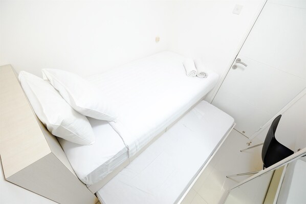 A clean, white room with a bed, a chair, and a small table.