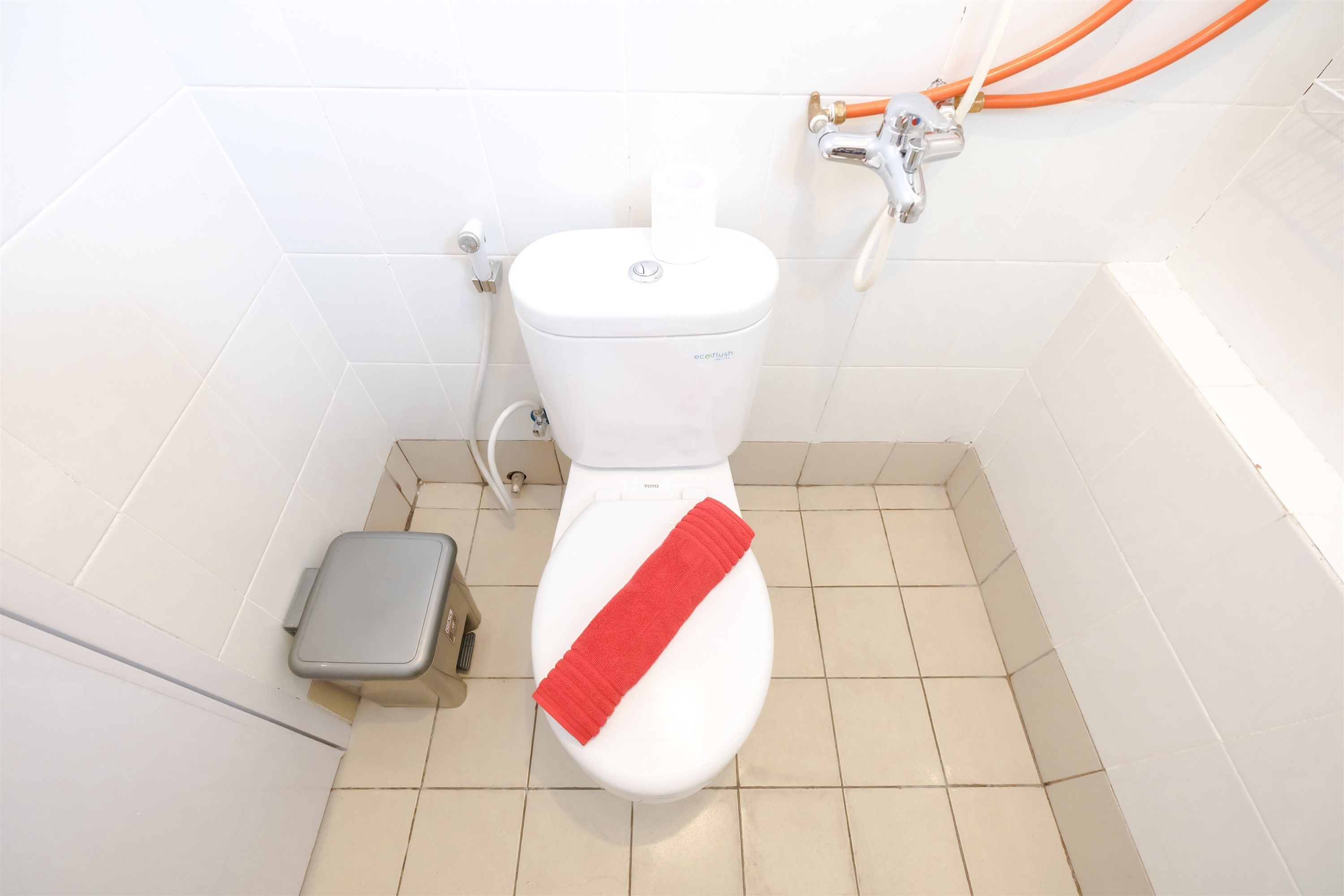A toilet with a red towel, a small trash bin, and a visible toilet paper holder.