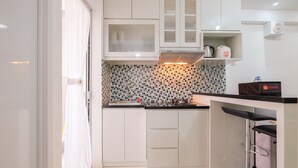 A modern kitchen with white cabinets, a tiled backsplash, and a bar area with stools. - Minimalist Bassura Apartment Direct Access to Bassura City Mall (Jakarta)