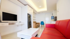 Una sala de estar moderna con un televisor de pantalla plana, una mesa de centro blanca, un sofá rojo, un sofá beige y un sillón azul.