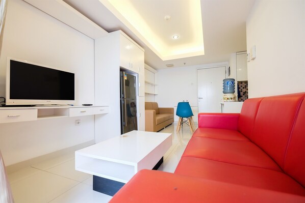 A modern living room with a flat-screen TV, a white coffee table, a red sofa, a beige sofa, and a blue chair. - The Wave Apartment near Kota Kasablanka (Jakarta)