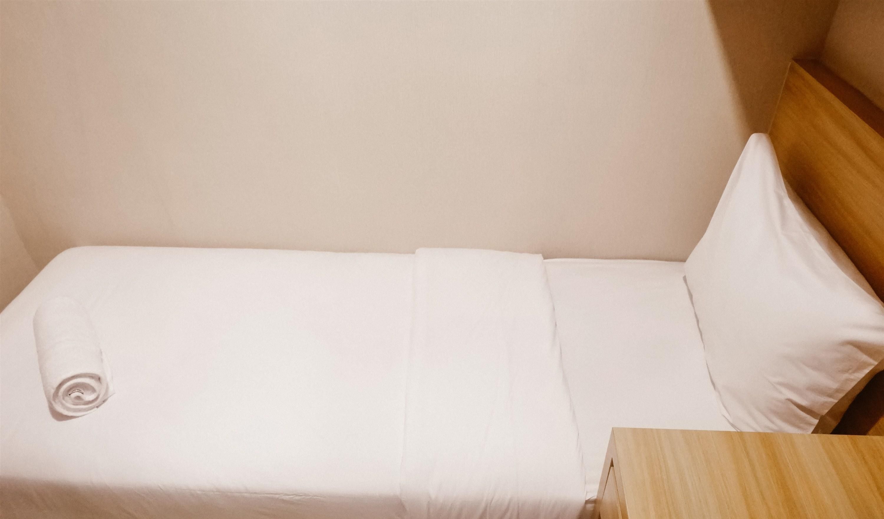 Un lit simple avec une literie blanche, une tête de lit en bois et une table de chevet en bois.