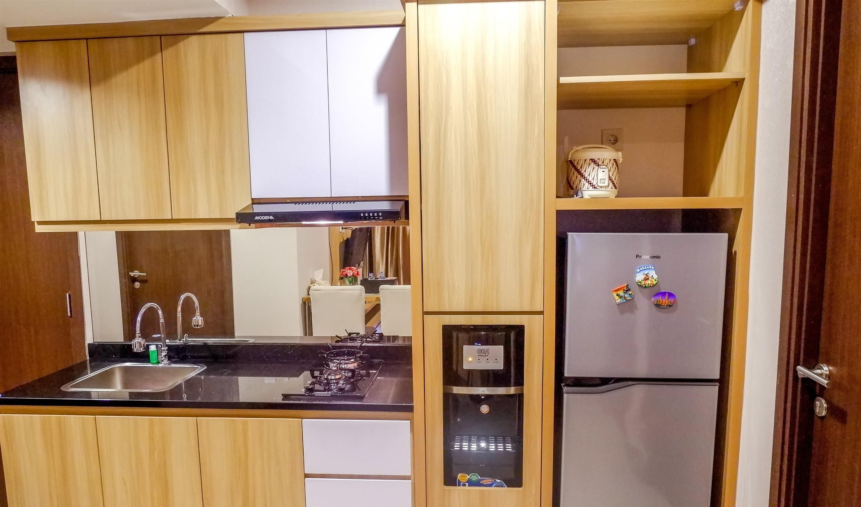 A compact kitchen with wooden cabinets, a stainless steel sink, a built-in oven, and a refrigerator with magnets.