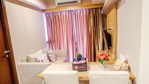 Een hotelkamer met een bank, een eettafel met een doosje met de tekst 'travelio', een vaas met bloemen en een tv aan de muur.
