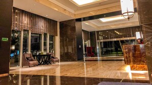 Un hall d’entrée moderne avec une cloison en verre, un espace salon et un lustre.