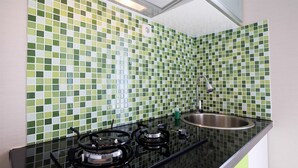 Eine Küche mit grünen und weißen Mosaikfliesen, einem Edelstahl-Spülbecken und einem Gasherd.