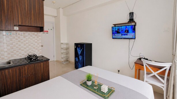 A modern kitchen with a gas stove, a refrigerator, and a flat-screen TV mounted on the wall. - Comfy Studio Apartment @ Green Pramuka City (Jakarta)