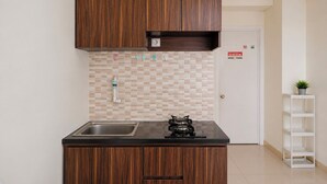 A compact kitchen with wooden cabinets, a stainless steel sink, and a tiled backsplash. - Comfy Studio Apartment @ Green Pramuka City (Jakarta)