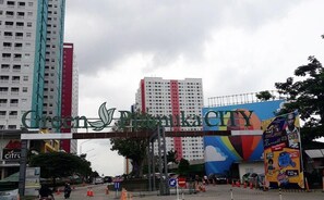 Une entrée de ville avec une grande enseigne indiquant « Green Pramuka City » et une fresque murale colorée.