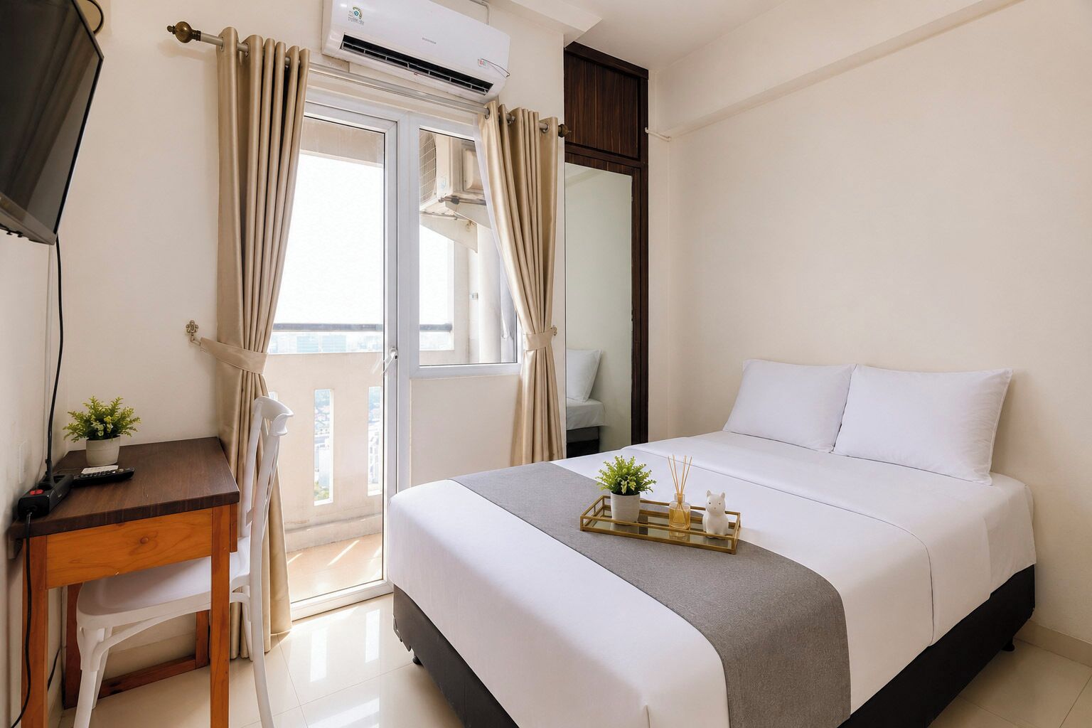 Habitación de hotel con cama, escritorio con planta, ventana con cortinas y unidad de aire acondicionado.