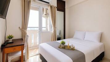 Habitación de hotel con cama, escritorio con planta, ventana con cortinas y unidad de aire acondicionado.