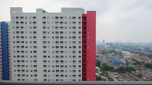 A multi-story residential building with balconies, a parking area, and a view of a cityscape in the background. - Comfy Studio Apartment @ Green Pramuka City (Jakarta)