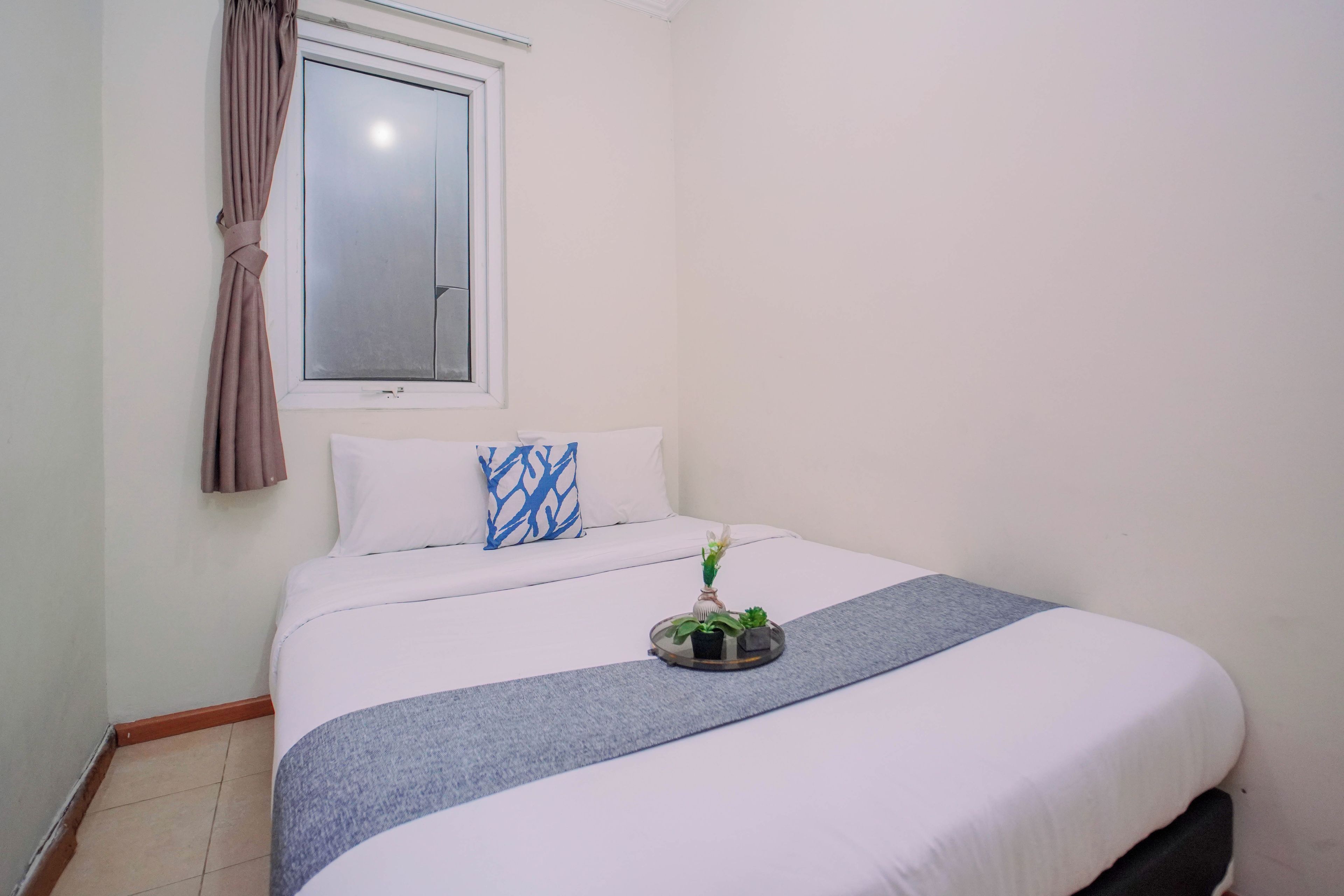A bedroom with a bed, a window with curtains, and a small plant on the bed.
