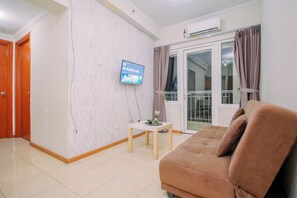 A living room with a sofa, a television mounted on the wall, a small table with a plant, and a sliding glass door leading to a balcony.