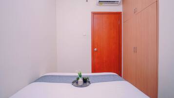 Un dormitorio con cama, armario de madera, puerta y aire acondicionado de pared.