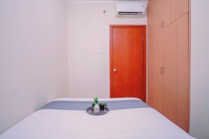 A bedroom with a bed, a wooden wardrobe, a door, and a wall-mounted air conditioner. - Apartment Palazzo/Grand Palace Kemayoran (Jakarta)