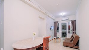 A living room with a brown sofa, a dining table with chairs, and a TV mounted on the wall. - Apartment Palazzo/Grand Palace Kemayoran (Jakarta)