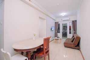 A living room with a sofa, a dining table with chairs, a TV mounted on the wall, and a sliding glass door leading to an outdoor area. - Apartment Palazzo/Grand Palace Kemayoran (Jakarta)