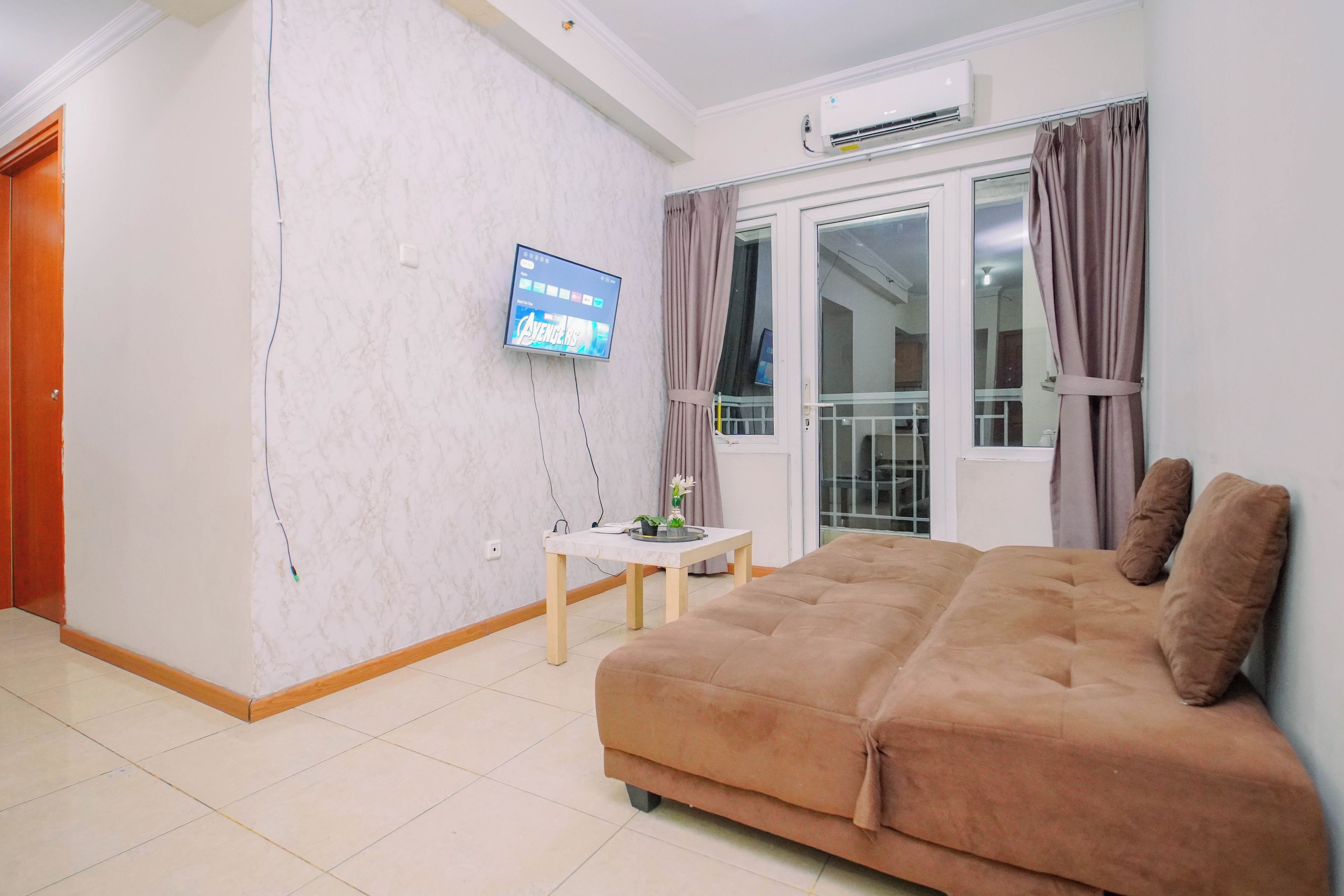 A living room with a sofa, a television mounted on the wall, a small table with a plant, and a window with curtains.