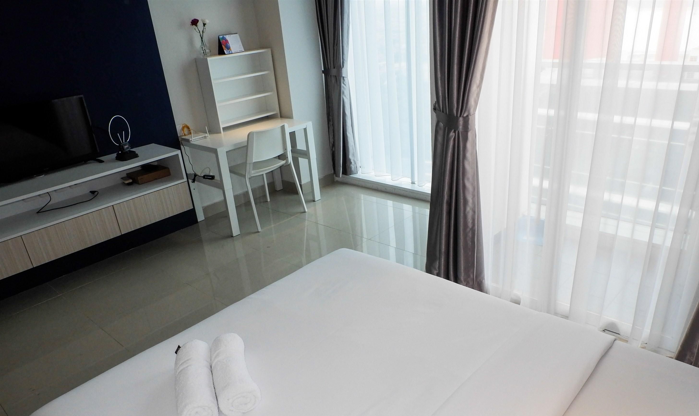 A hotel room with a bed, a desk, a TV, and a window with curtains.