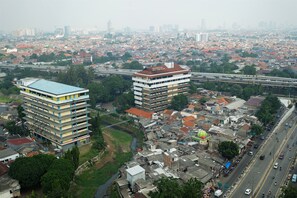 An aerial view of a cityscape with dense residential buildings, a prominent university building, and a highway with vehicles. - Luxurious Bassura City Apartment with Mall Access (Jakarta)